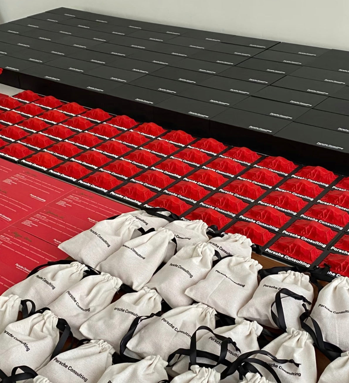 Premium 3D printed corporate gifts by owl3dmesh for Porsche Consulting, packaged in black and red boxes and white drawstring bags, are arranged in a precise grid to showcase their empowering brand value.