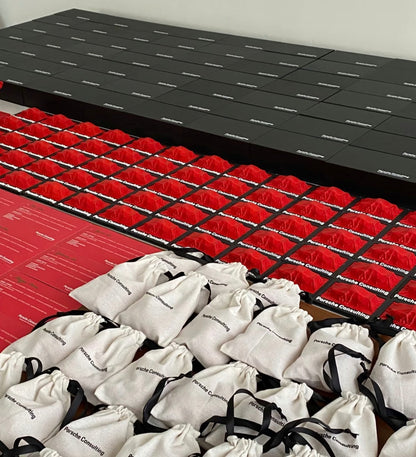 Premium 3D printed corporate gifts by owl3dmesh for Porsche Consulting, packaged in black and red boxes and white drawstring bags, are arranged in a precise grid to showcase their empowering brand value.